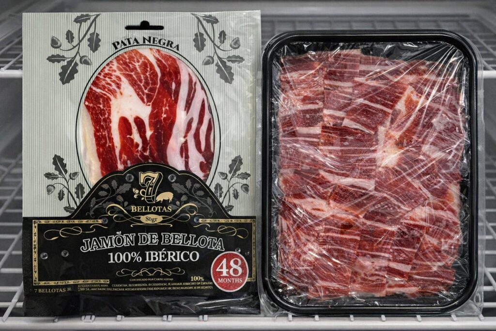 A close-up of a 7Bellotas vacuum-sealed sliced pack sitting next to an open pack that has been carefully covered in clear cling film, resting on a refrigerator shelf